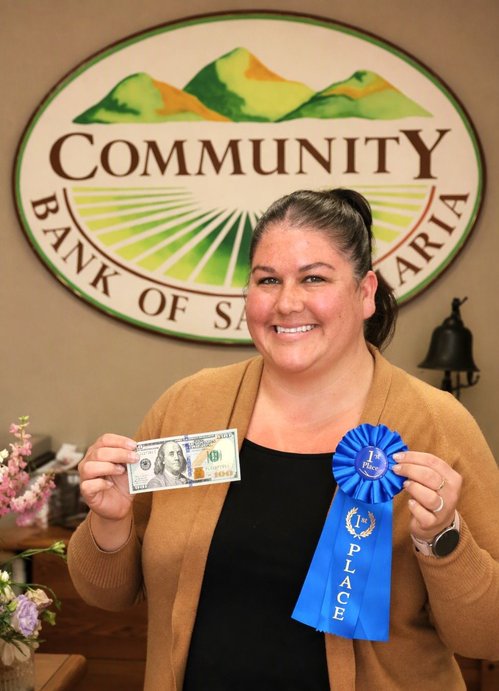 Image of woman holding blue first place ribbon and 100 dollar bill in front of Community Bank of Santa Maria sign